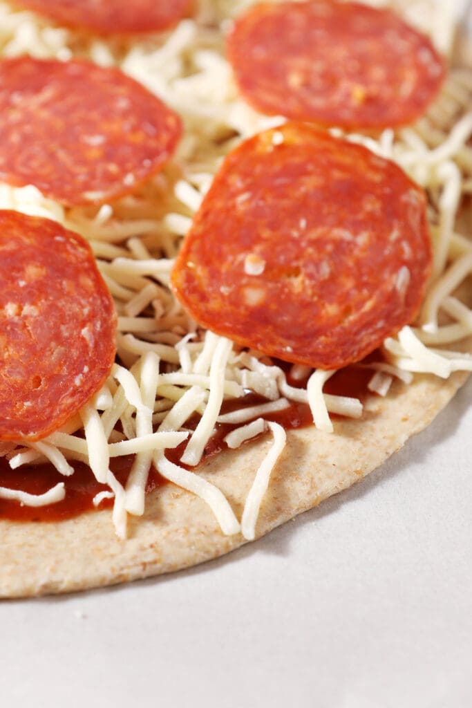 Close up of pizza dough topped with sauce, cheese and pepperoni on parchment before baking