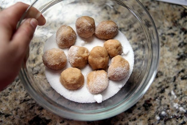 A hand holds a bowl holding peanut butter cookie balls with granulated sugar