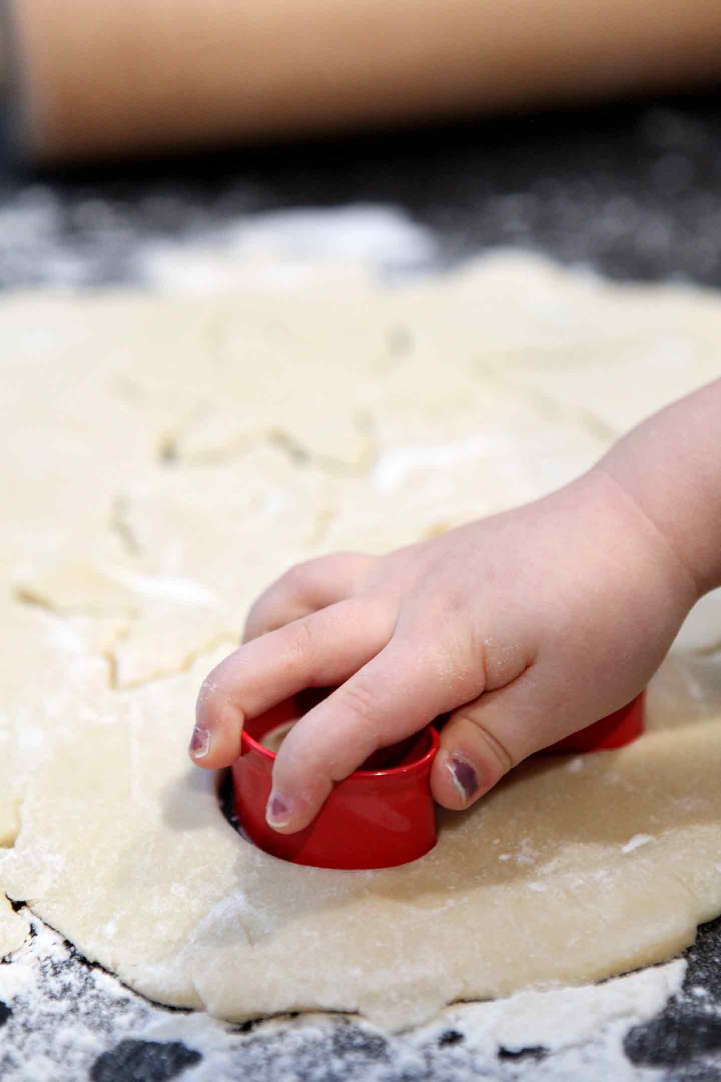 A child uses a cookie cutter to make a All-Butter Tea Cake Cookies in a round of rolled out cookie dough