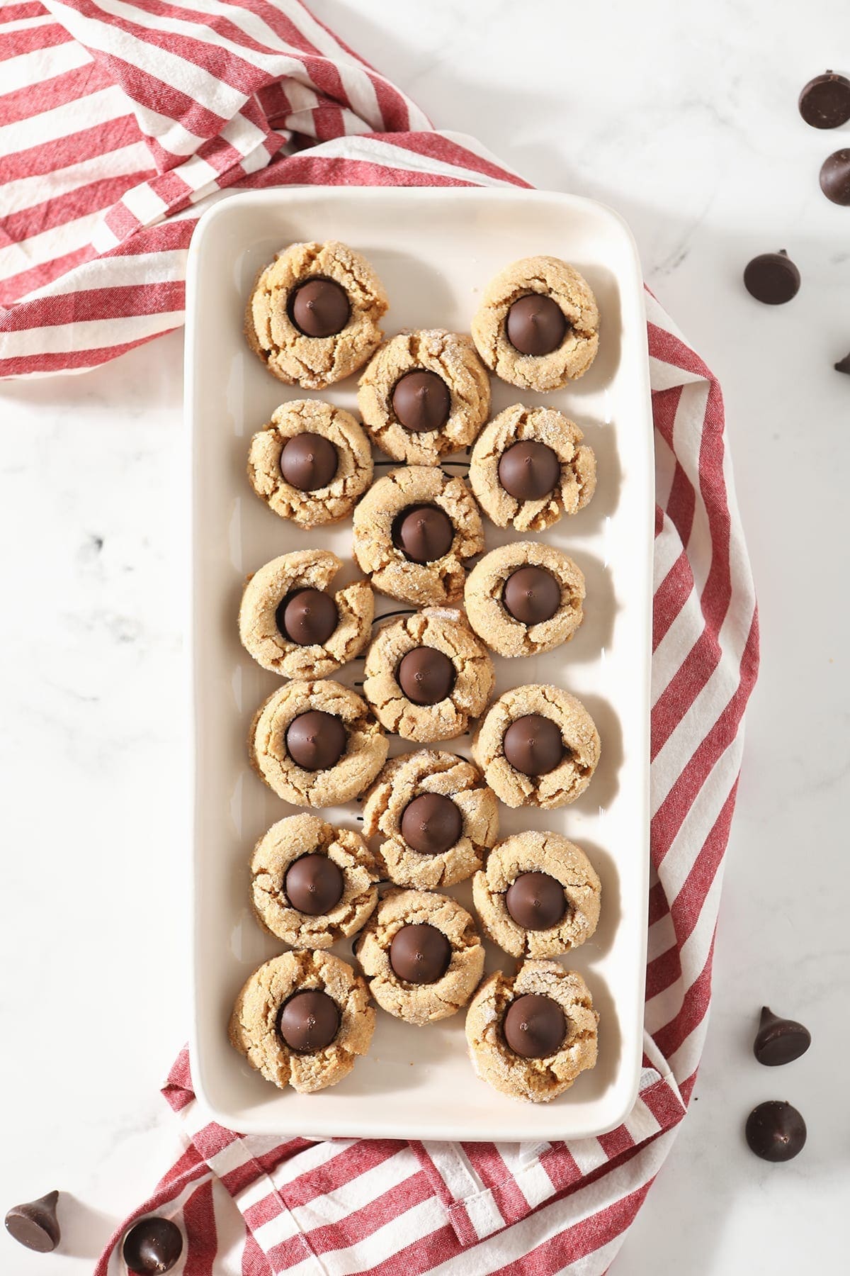 A tray of Dark Chocolate Peanut Blossom Cookies from above sitting on top of a red and white striped towel on a marble countertop