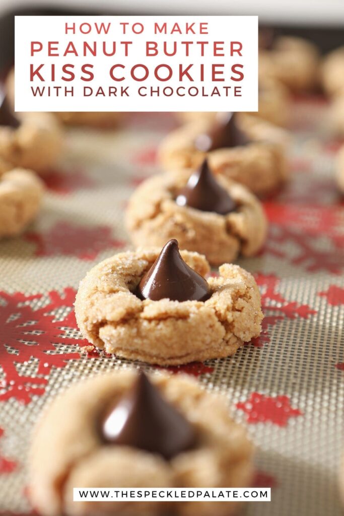 A row of baked peanut butter cookies with hershey's kisses on a sheet pan with the text 'how to make peanut butter kiss cookies with dark chocolate'