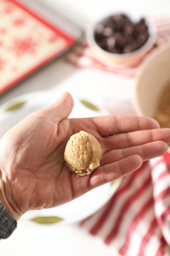 A hand holds a ball of peanut butter cookie dough