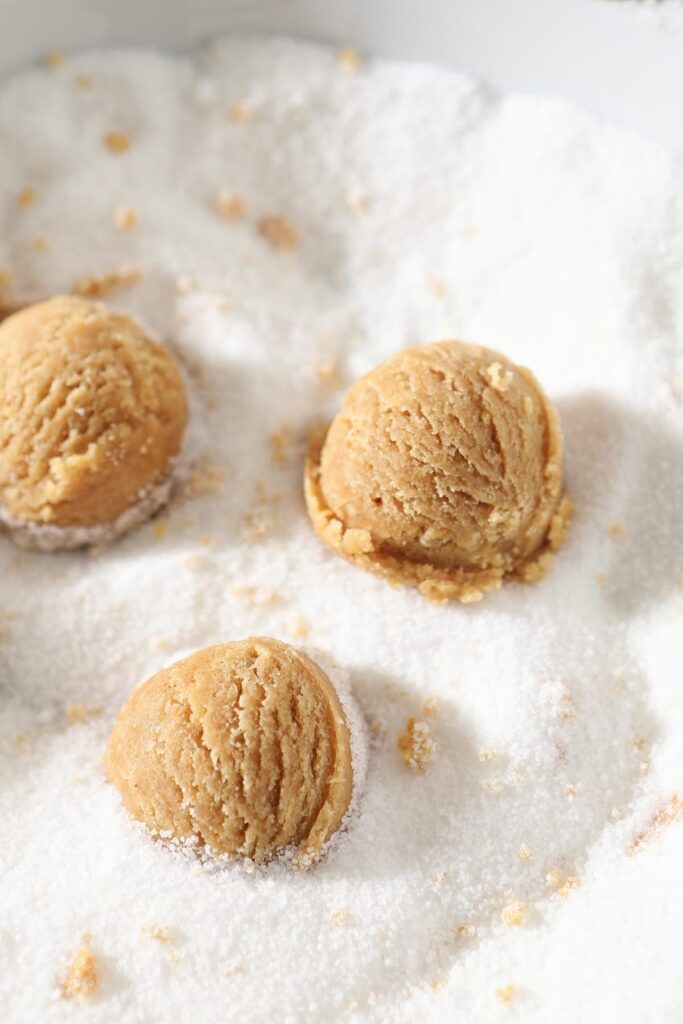 Three Peanut Blossom dough balls in a bowl of granulated sugar