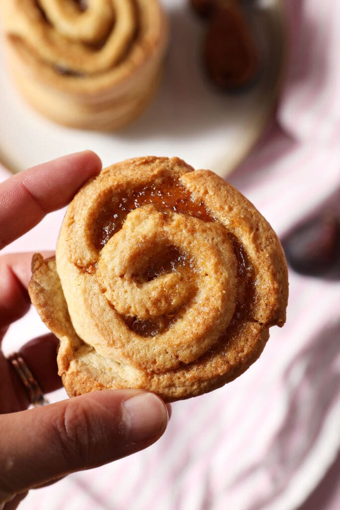 a hand holds a rolled fig cookie above a pink surface