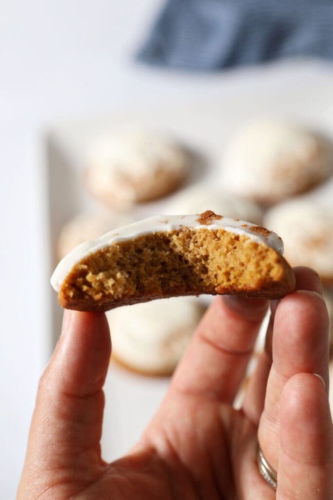 A bitten-into Pumpkin Cookie with Cream Cheese Frosting held in hand above a plate of cookies