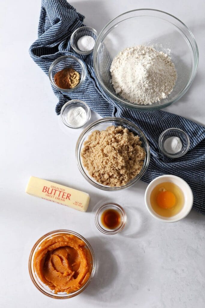 Ingredients to make pumpkin cookies on a white stone surface with a blue towel