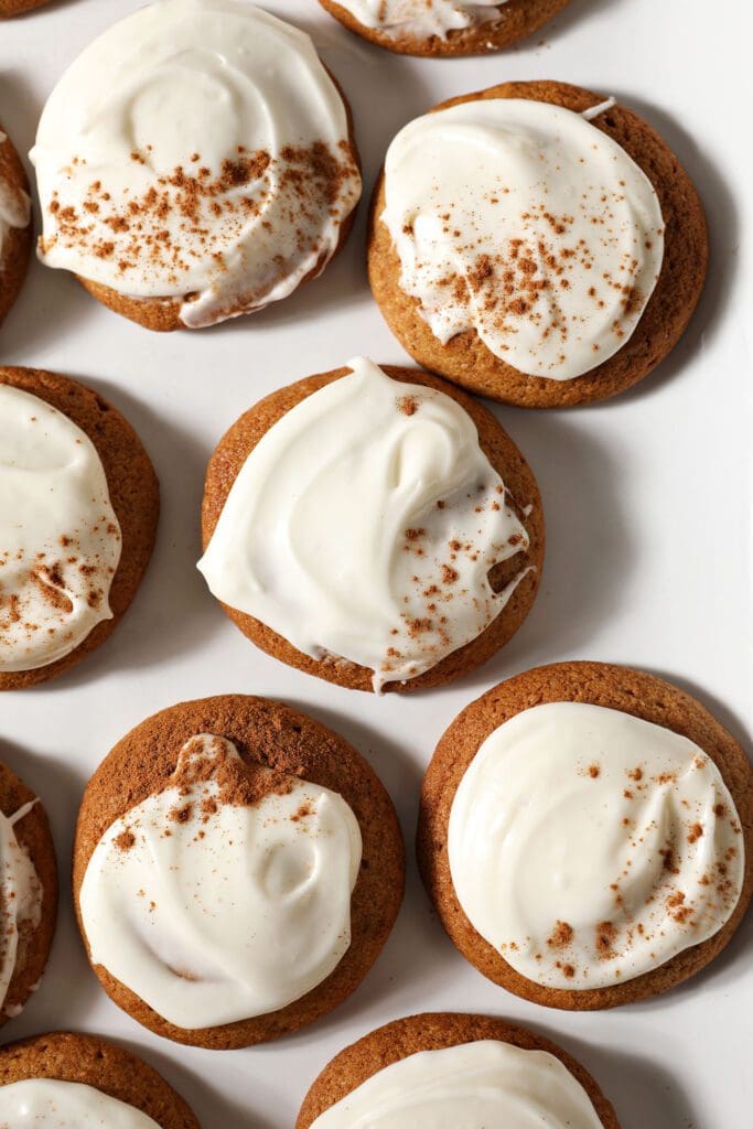 Several Pumpkin Cookies with Cream Cheese Frosting sprinkled with cinnamon on a white plate