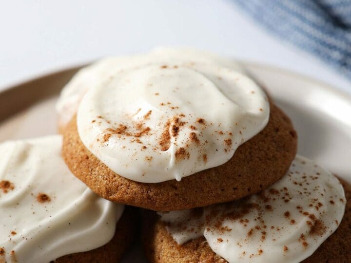 A small plate stacked with Pumpkin Cookies with Cream Cheese Frosting with a blue towel in the background