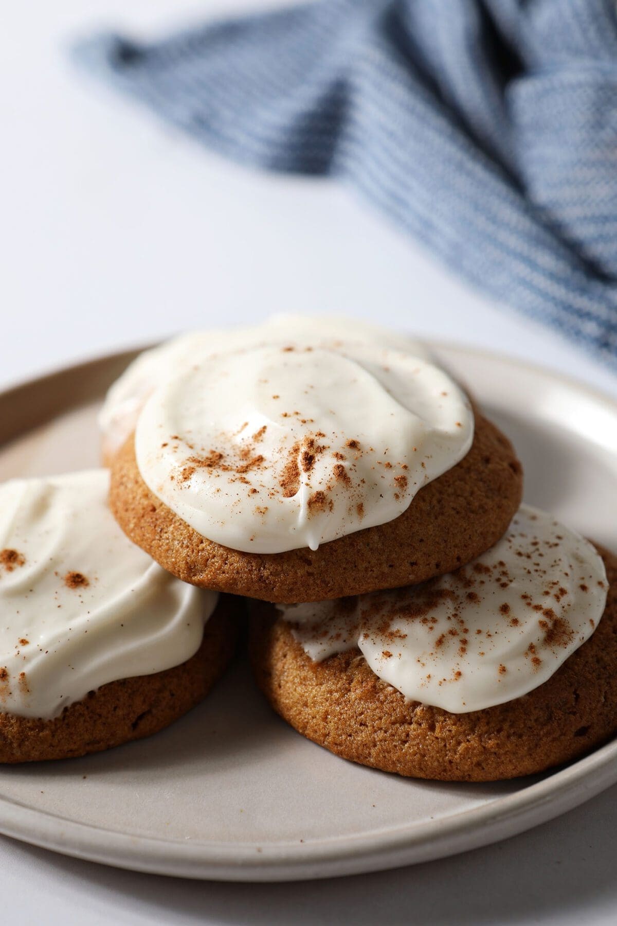 A small plate stacked with Pumpkin Cookies with Cream Cheese Frosting with a blue towel in the background