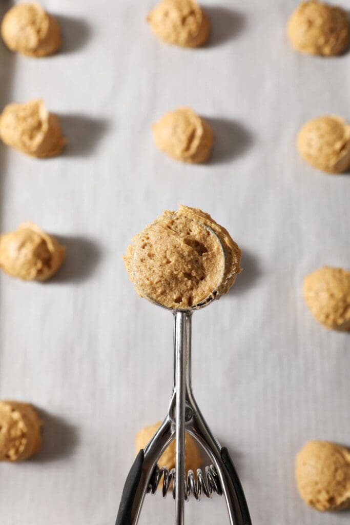 A small scoop holds cookie batter above a sheet pan of cookies