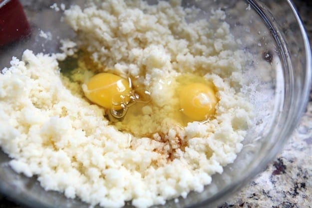 Two eggs on top of a butter-sugar mixture in a clear glass bowl