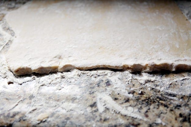 Close up of cookie dough rolled flat on a floured countertop