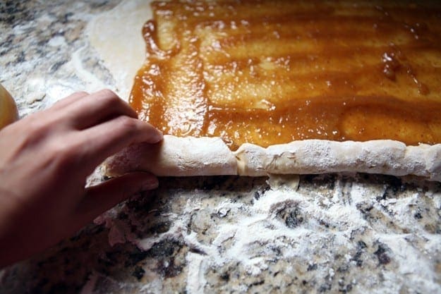 A hand rolls cookie dough with fig preserves into a log to form pinwheel cookies