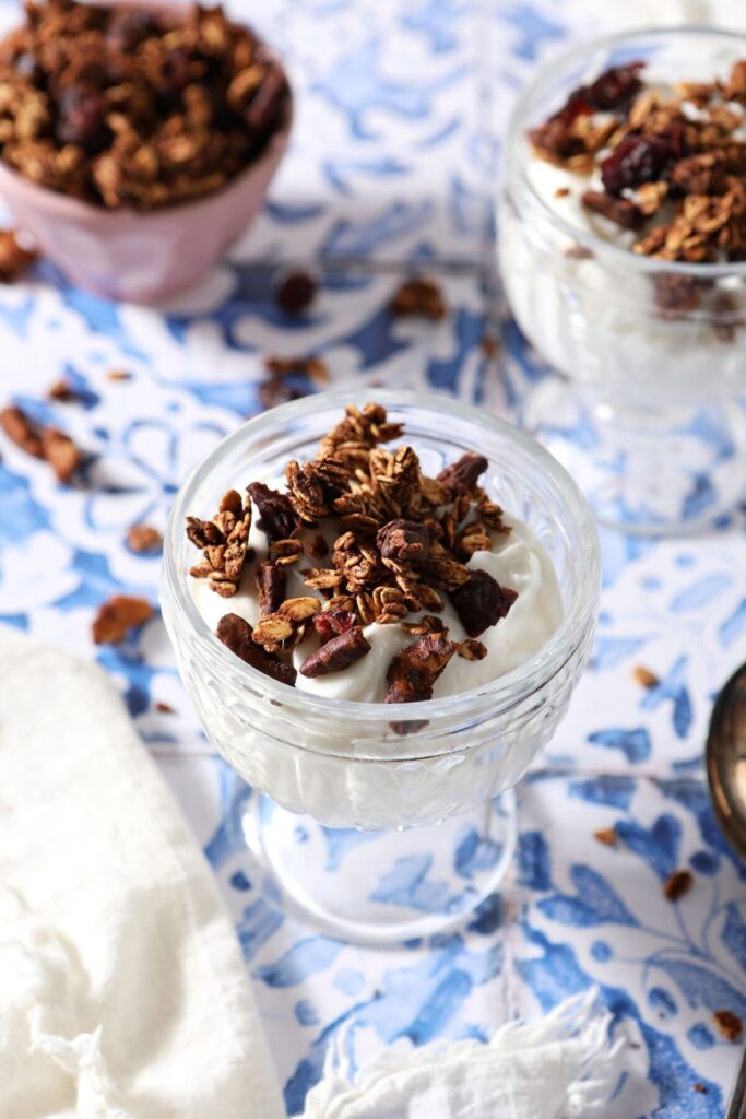 Two glass containers of yogurt topped with homemade granola on a tiled surface