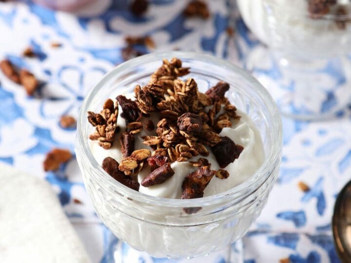 Two glass containers of yogurt topped with homemade granola on a tiled surface