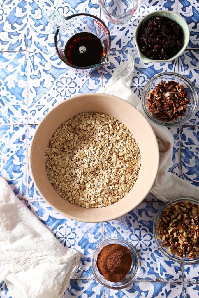 Bowls of ingredients to make maple nut granola on a blue tile surface