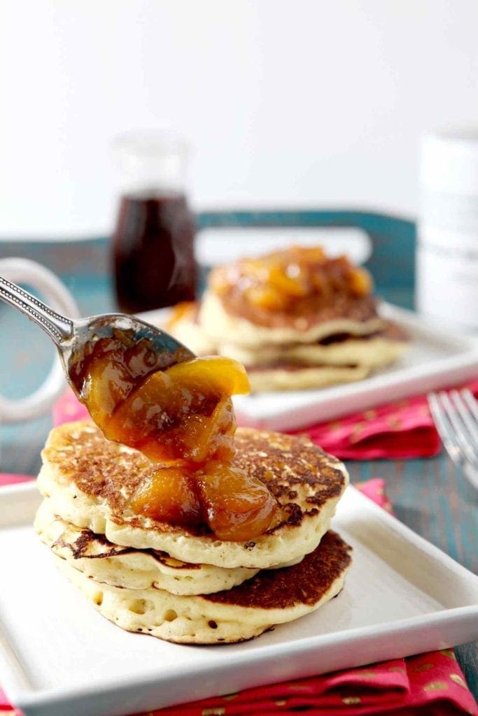 Compote is dolloped on top of a stack of pancakes with a spoon