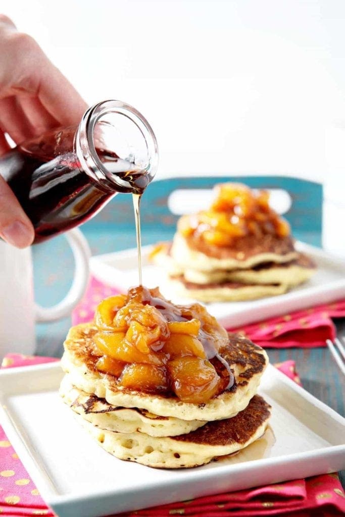 Maple syrup pours over Peach Compote on top of pancakes