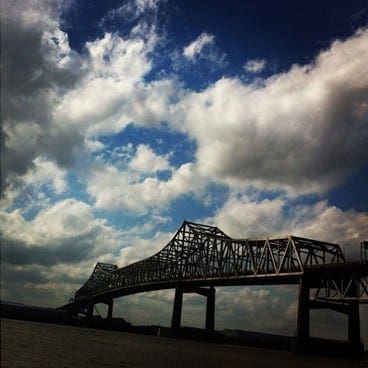 A blue cloudy sky behind a metal bridge over water 