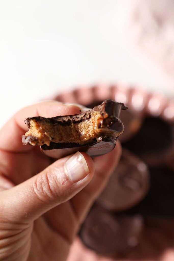 A bitten-into peanut butter cup held in a hand above a pink plate 