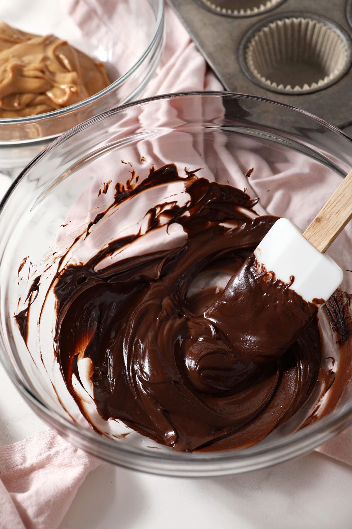 Melted chocolate in a large bowl with a white rubber spatula on marble