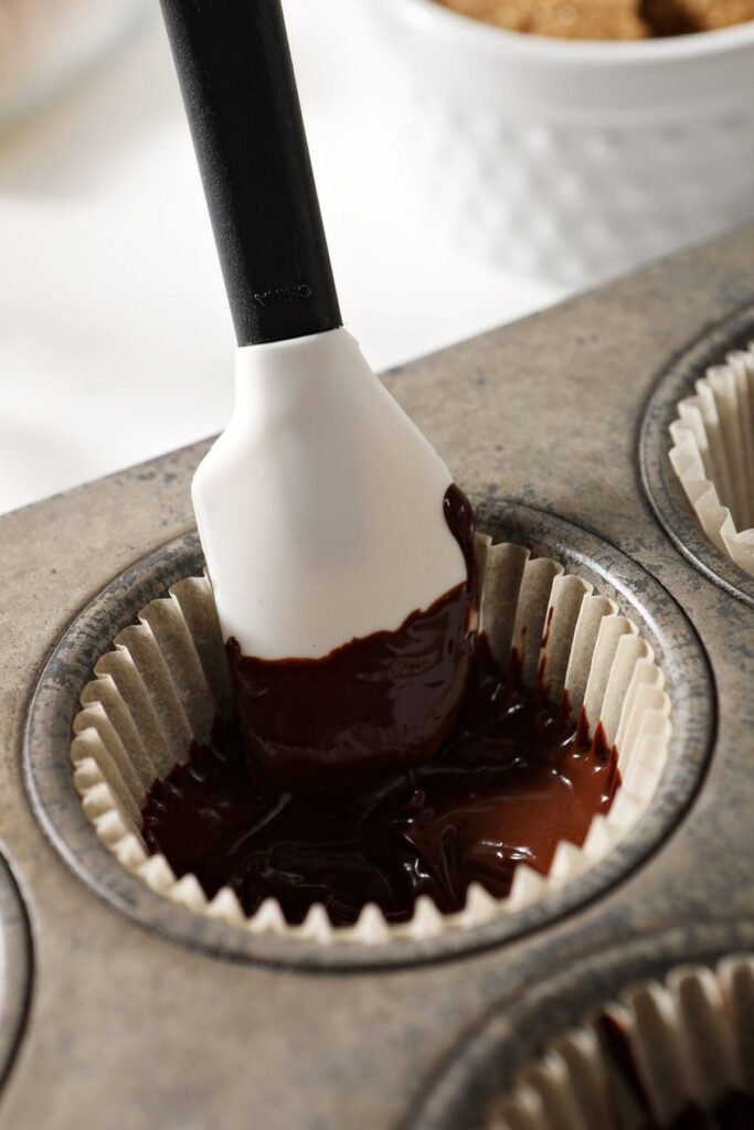 A small rubber spatula spreads warm chocolate up the side of a muffin liner