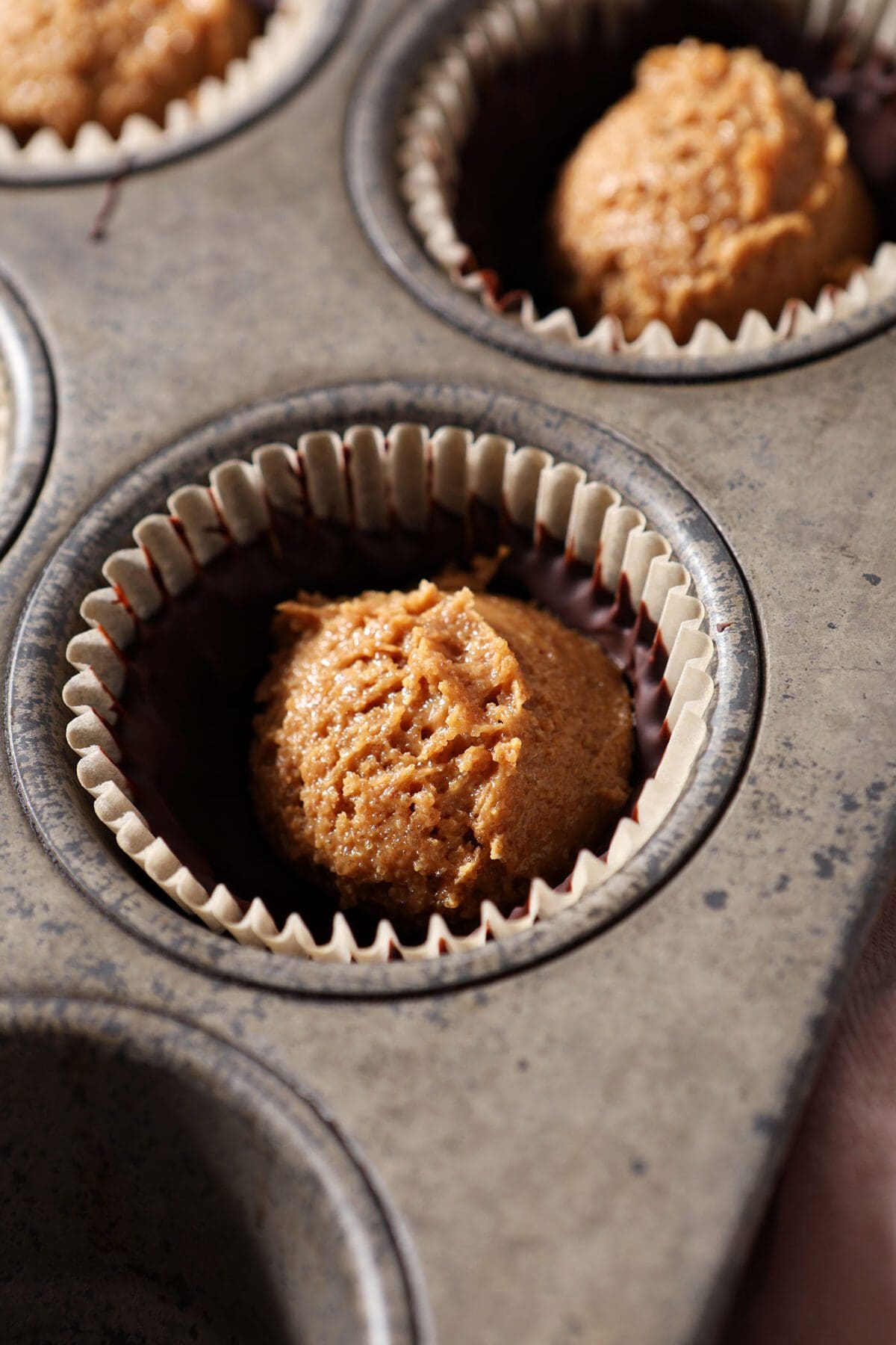 A scoop of peanut butter filling inside homemade chocolate shells in a muffin tin