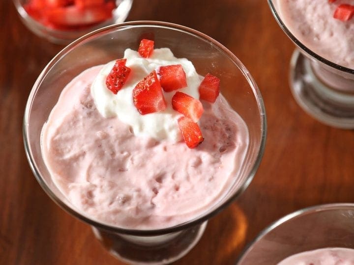 A wooden tray holds cups of pudding garnished with yogurt and chopped strawberries