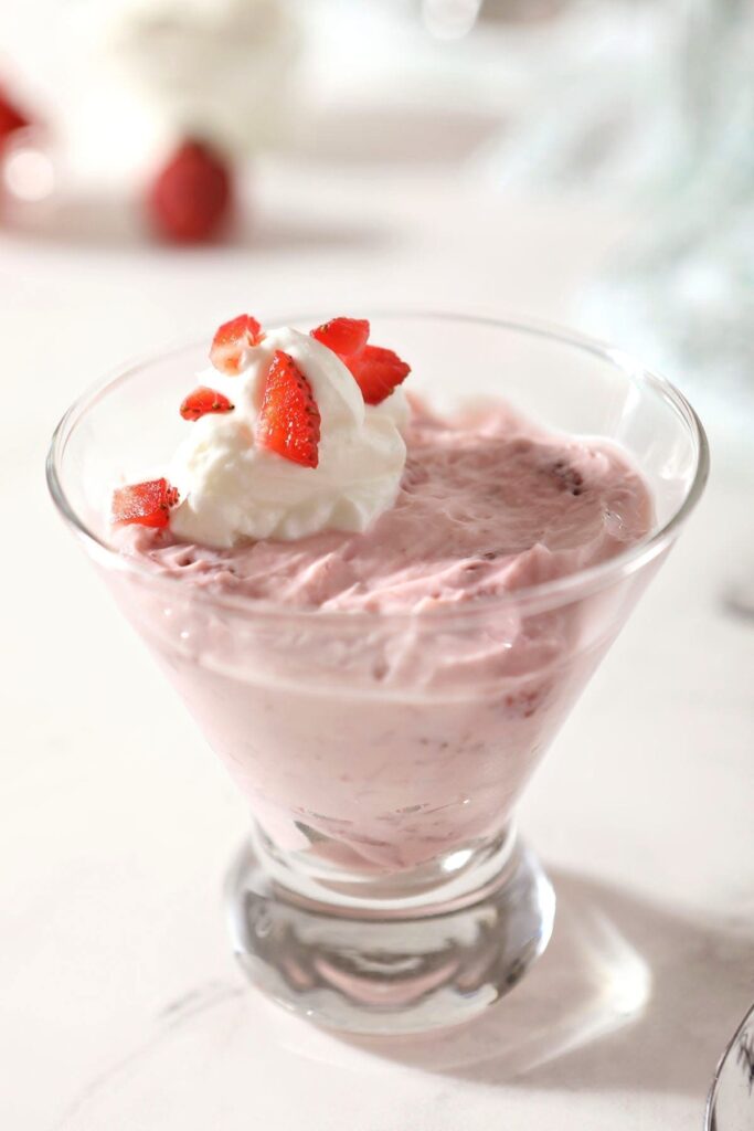 A martini cup holds a serving of pudding garnished with yogurt and chopped strawberries