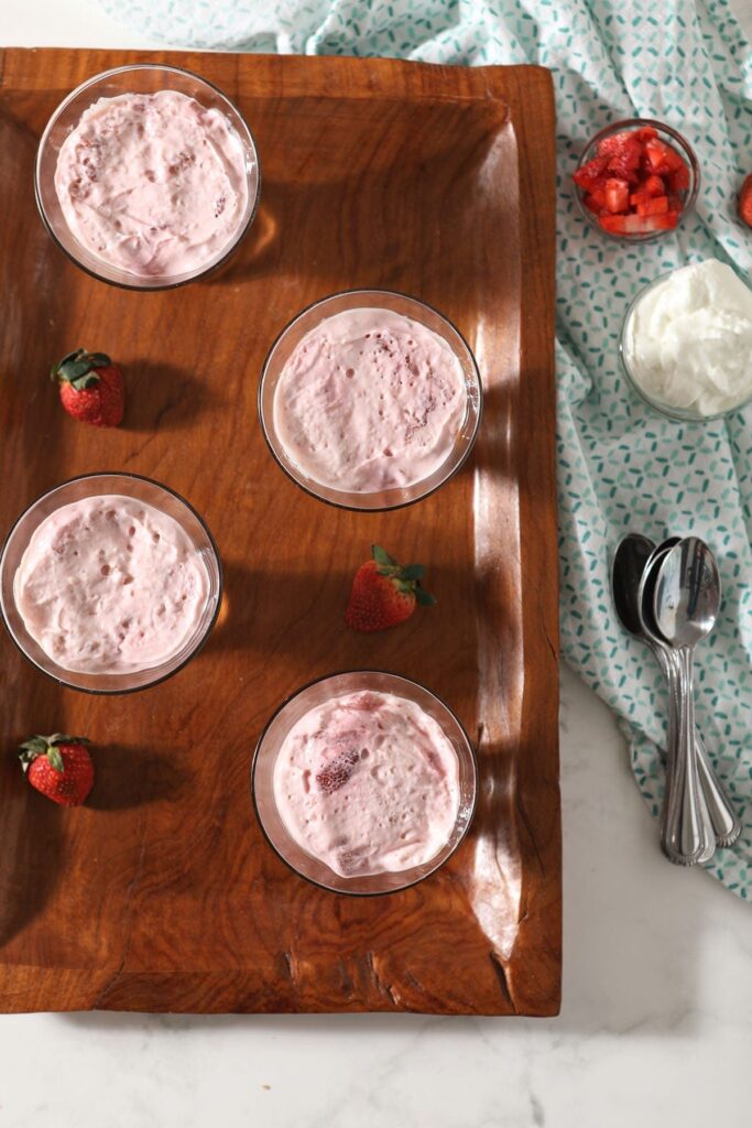 Four servings of strawberry pudding in bowls on a wooden tray before garnishings are added