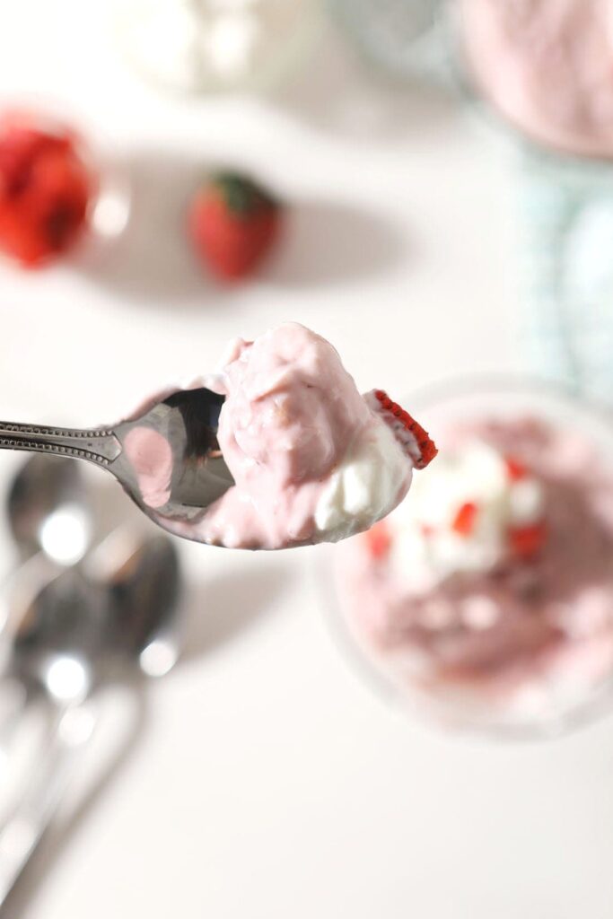 A spoon holds a bite of strawberry pudding above a bowl of it