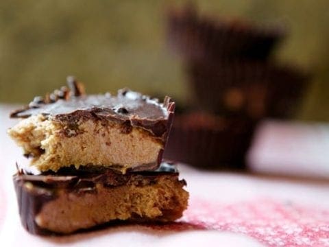 A halved Dark Chocolate Peanut Butter Cup on a pink towel with a stack of the cups behind it