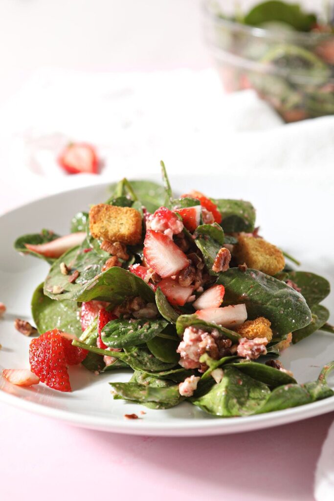 A strawberry spinach salad on a white plate tossed with strawberry vinaigrette