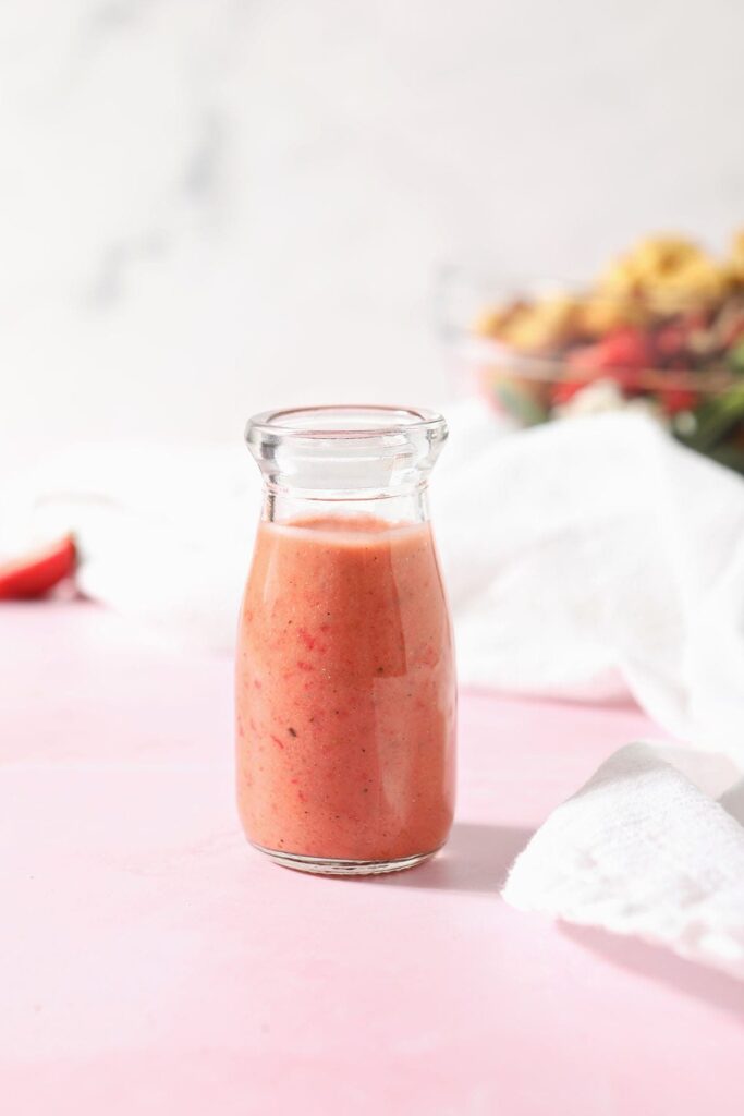 A bottle of strawberry vinaigrette sits in front of a salad bowl