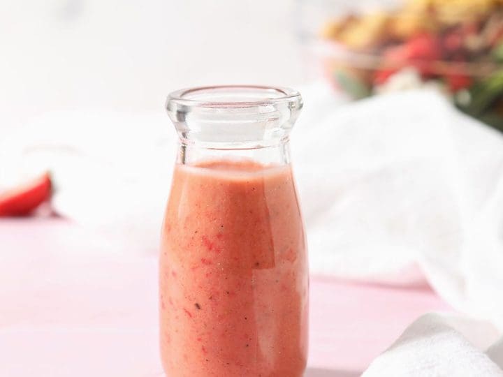 A bottle of strawberry vinaigrette sits in front of a salad bowl