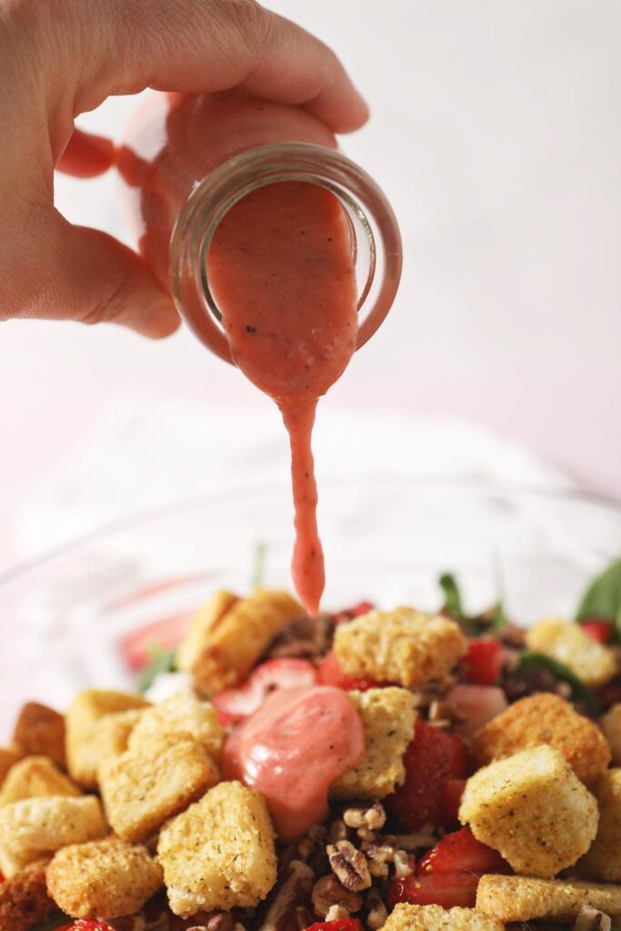 Strawberry salad dressing drizzles on top of a salad with croutons, cheese and more