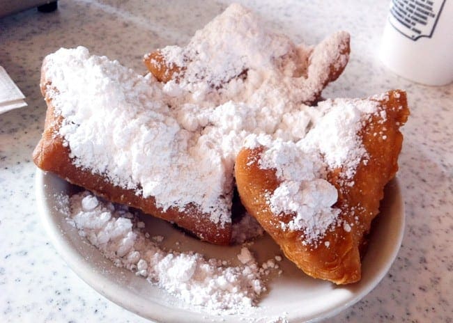 A white plate of three beignets coated in powdered sugar