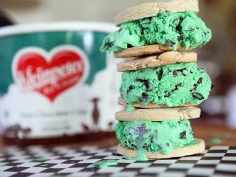 Three stacked mint chocolate chip ice cream sandwiches in front ice cream container