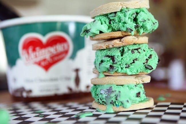 Three stacked mint chocolate chip ice cream sandwiches in front ice cream container 