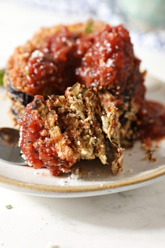 A fork holds a large bite of crispy eggplant next to a stack of the eggplant