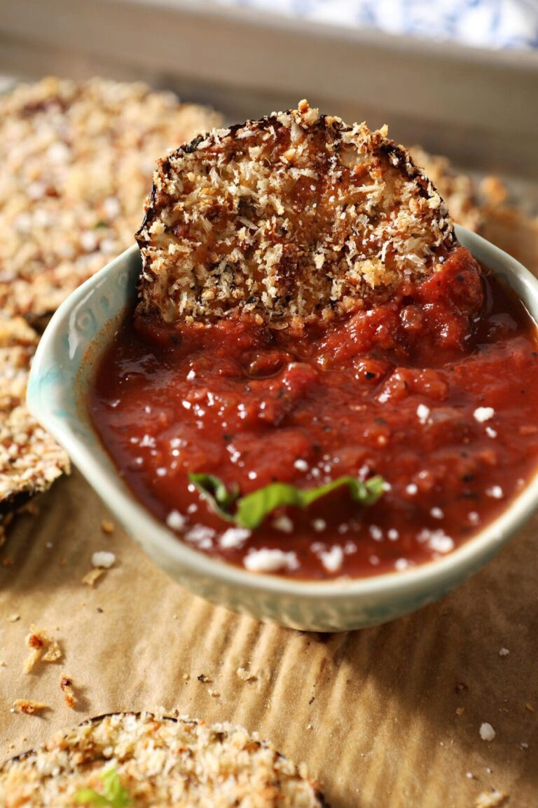 A crunchy eggplant medallion sits on a bowl of marinara sauce on a sheet pan