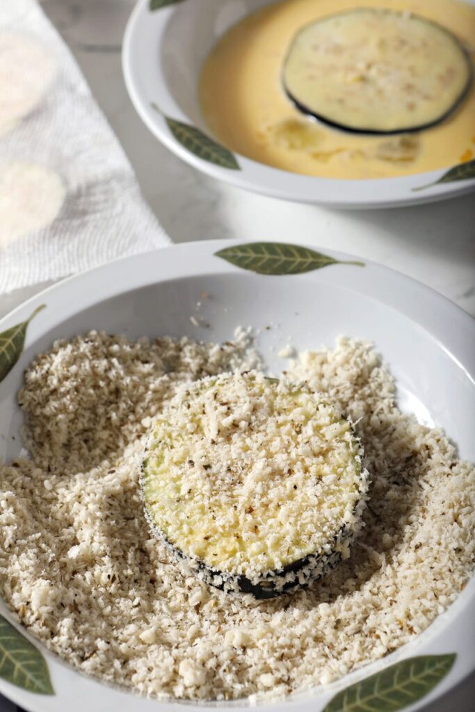 An eggplant slice sits in a bowl of panko and cheese