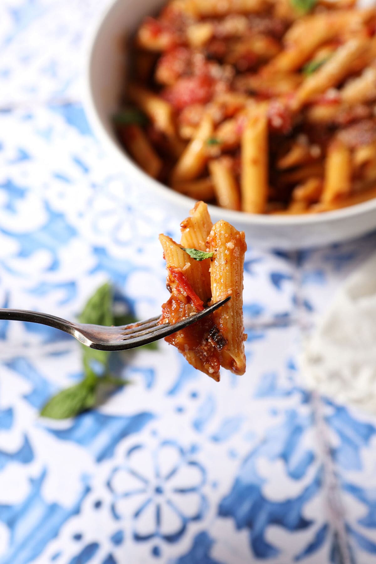 A fork holds a few penne coated in a tomato sauce over a blue and white tiled surface