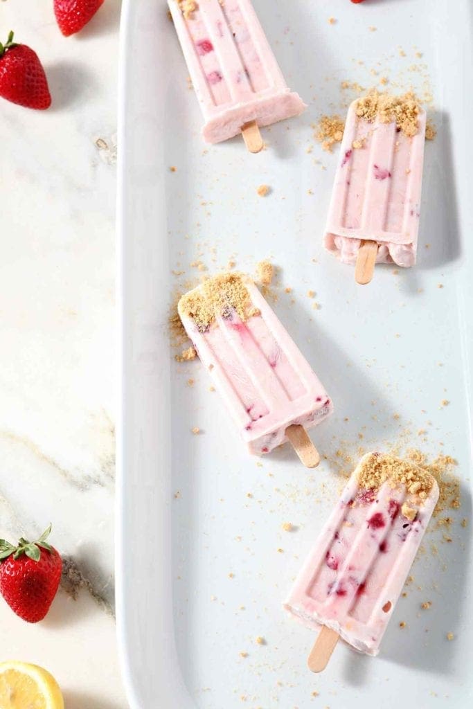 Four Roasted Strawberry Cheesecake Popsicles are shown from above on a white platter on a marble background