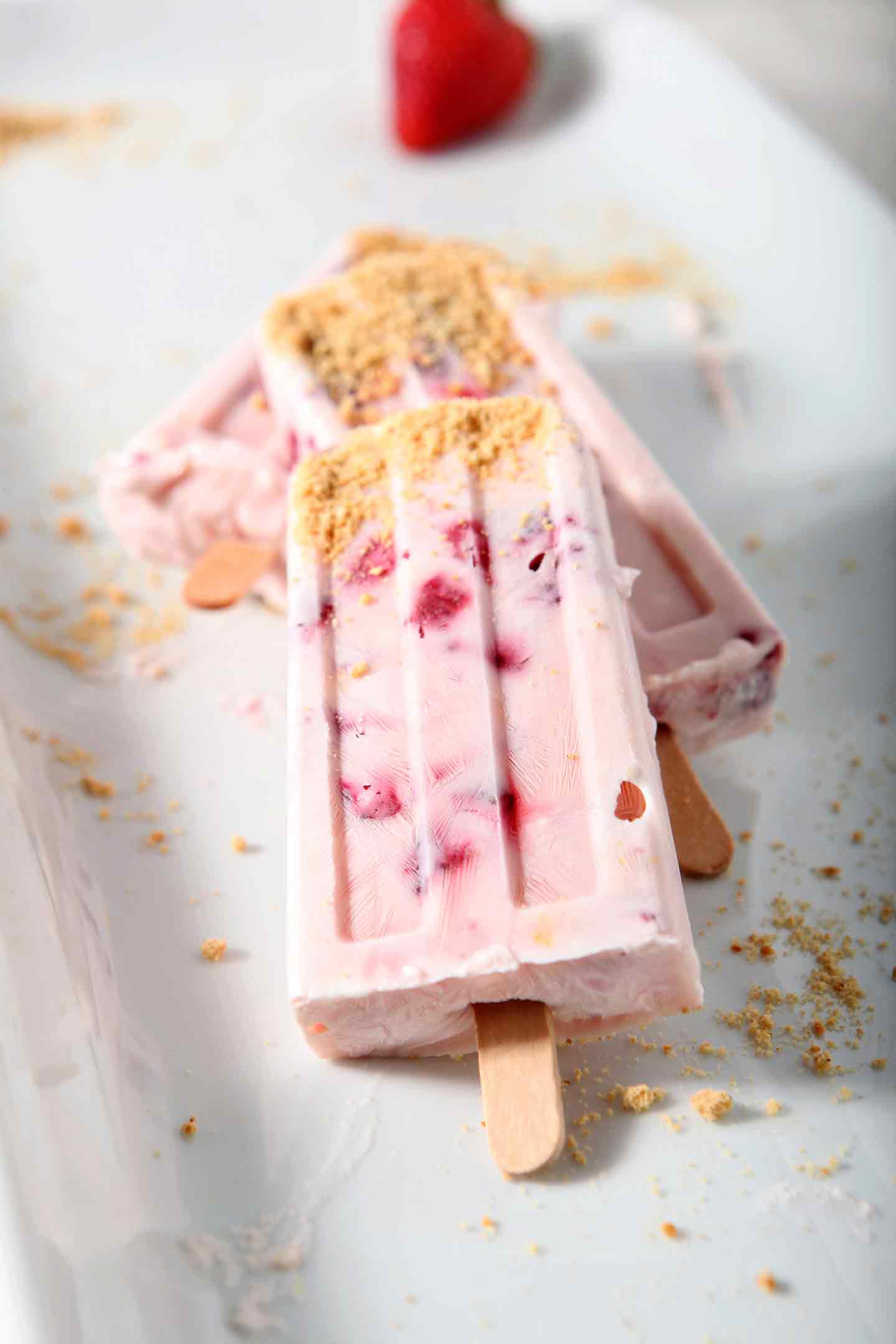 Several Roasted Strawberry Cheesecake Popsicles are stacked on top of each other on a white platter