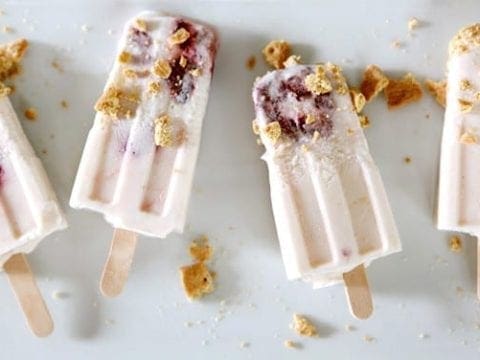 Four Roasted Strawberry Cheesecake Pops on a white platter with graham cracker sprinkles