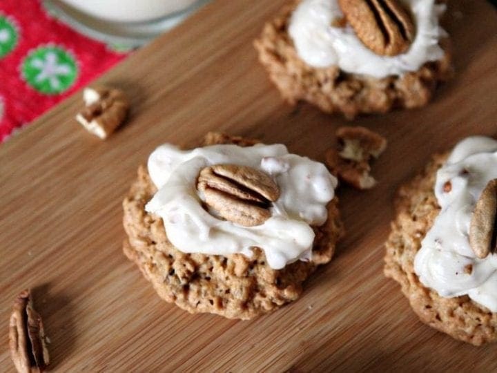 A wooden platter holds several Quebec Maple Pecan Drop Cookies, with a glass of milk sitting in the background