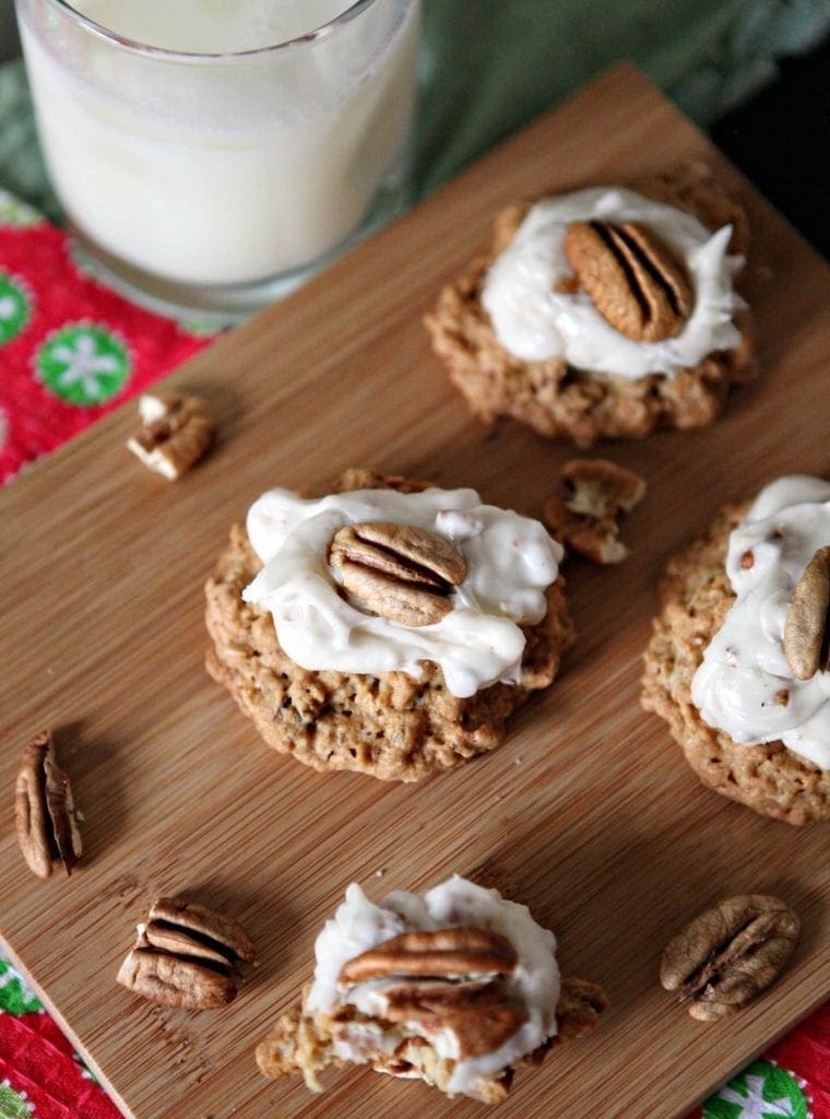 A wooden platter holds several Quebec Maple Pecan Drop Cookies, with a glass of milk sitting in the background