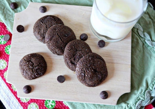 Five Chewy Chocolate Gingerbread Cookies lean against each other on a light wooden cutting board over red and green cloths
