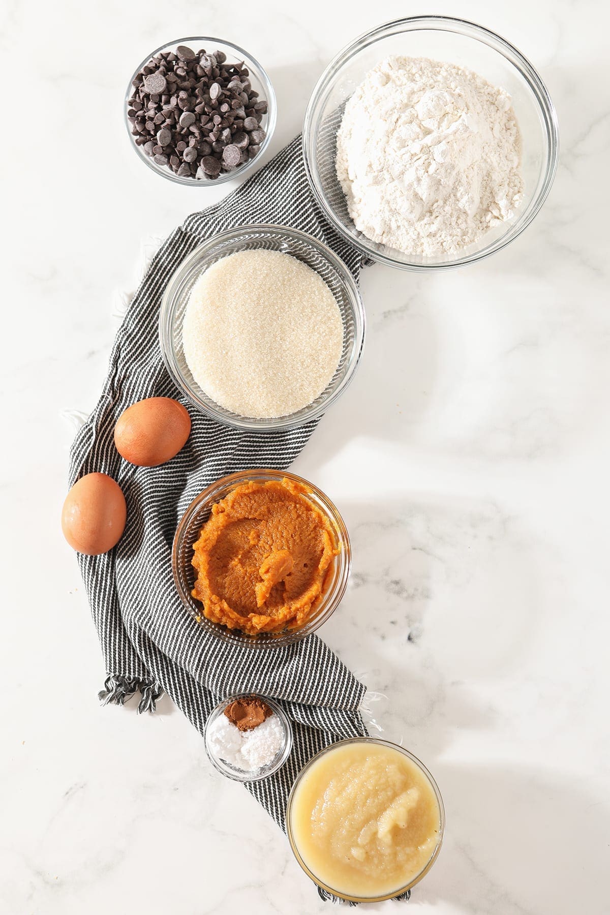 Ingredients for pumpkin bread recipe on a gray striped towel on marble